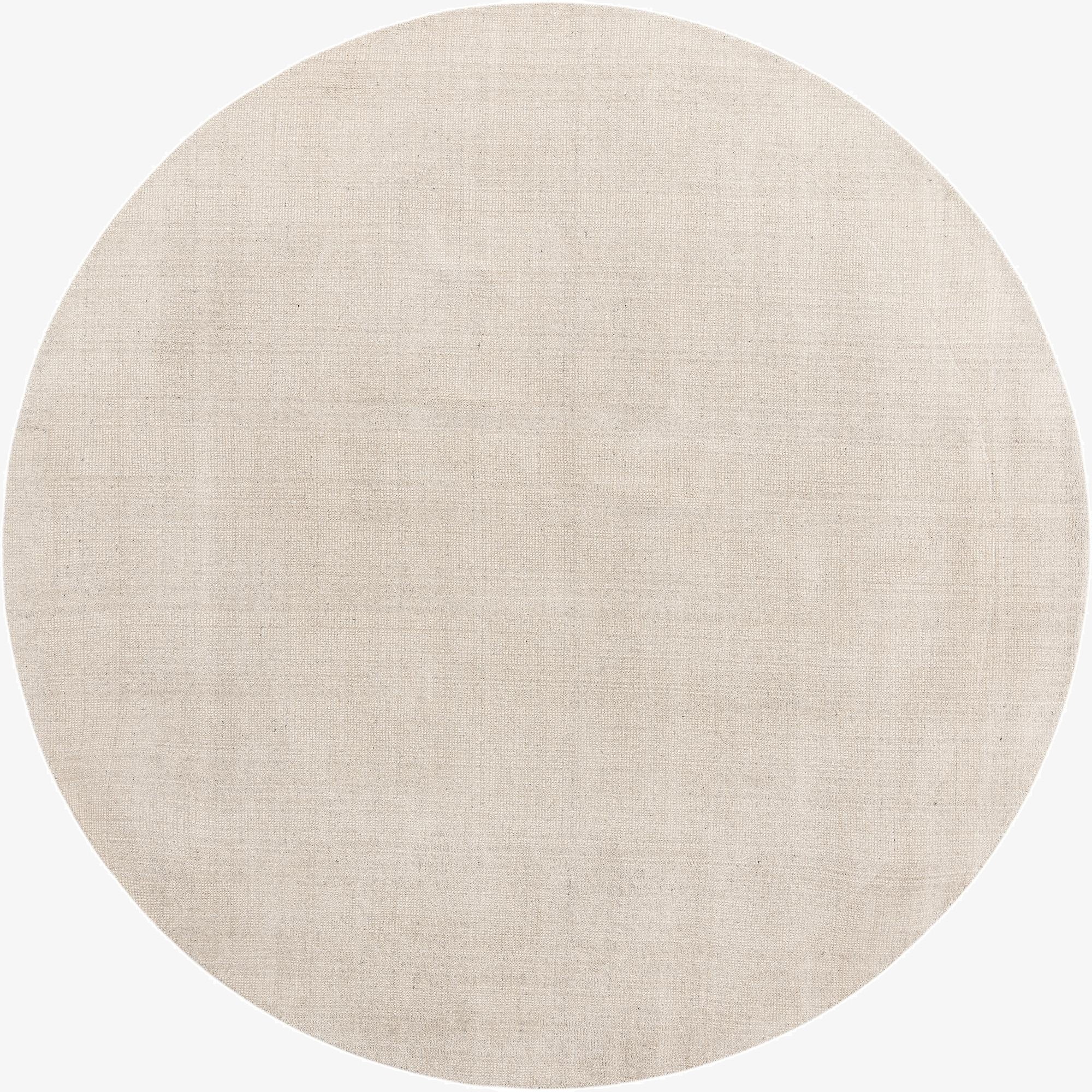 A 10-foot round Jill Zarin English Manor rug in a light brown, cream, and white solid color, showcasing its textured wool surface.